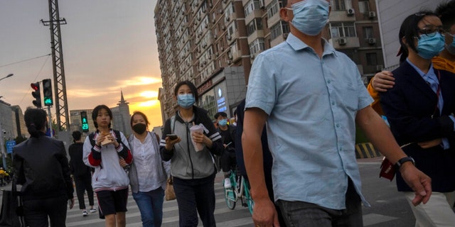 People wearing face masks walk across an intersection during the evening rush hour in Beijing, Wednesday, April 20, 2022. (AP Photo/Mark Schiefelbein)