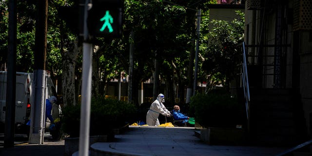 A worker in a protective suit helps a man in a wheelchair during lockdown amid the COVID-19 pandemic in Shanghai, China, May 5, 2022. 