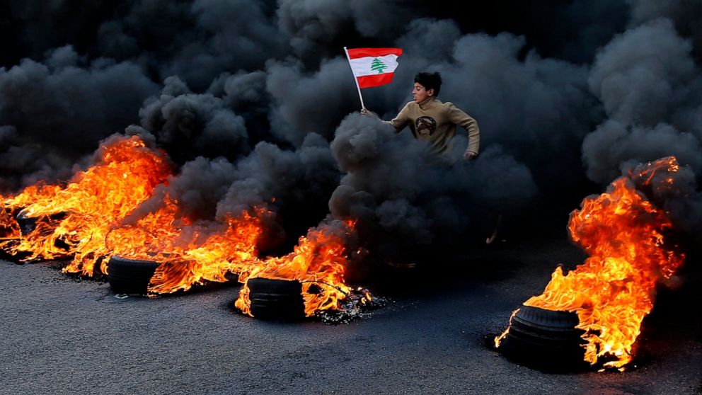 FILE- An anti-government demonstrator holds a national flag and runs across tires that were set on fire to block a main highway during a protest against a ruling elite they say has failed to address the economy's downward spiral, in the town of Jal e