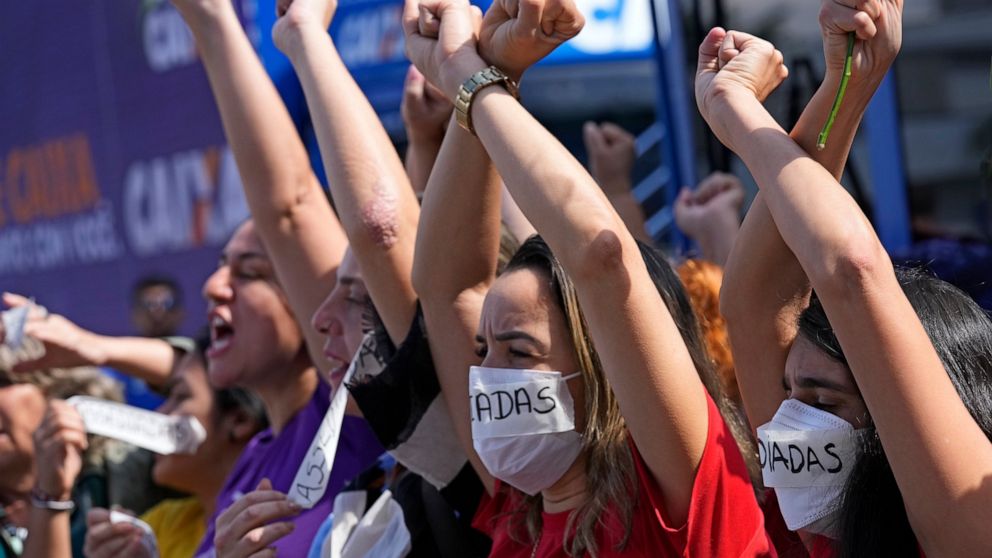 Employees of Caixa Economica Federal bank raise their arms and wear stickers over their mouths, that read "Harassment" in Portuguese, to protest the president of the institution Pedro Guimaraes after allegations of sexual harassment, outside the bank