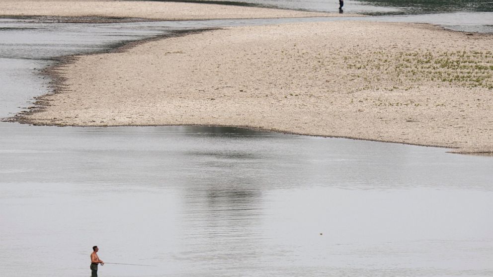 FILE - People fish near a hydroelectric power plant at Isola Serafini, on the Po river in San Nazzaro, Italy, Wednesday, June 15, 2022. The drying up of the river is jeopardizing drinking water in Italy's densely populated and highly industrialized d