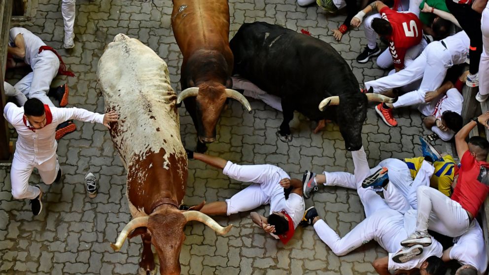 Runners fall during the running of the bulls at the San Fermin Festival in Pamplona, northern Spain, Monday, July 11, 2022. Revellers from around the world flock to Pamplona every year for nine days of uninterrupted partying in Pamplona's famed runni