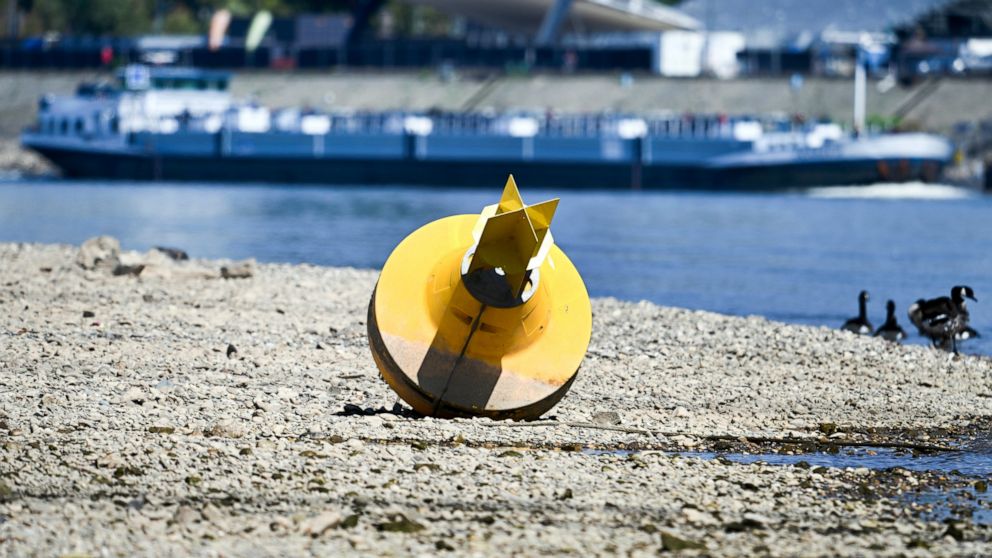 A cargo ship passes a danger buoy lying on dry land in Dusseldorf, North Rhine-Westphalia, Germany. After weeks of drought, the water levels of the Rhine have reached historic lows. (Federico Gambarini/dpa via AP)