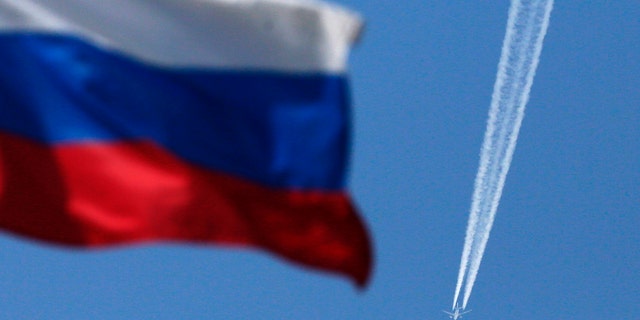 File photo - A contrail left by a passenger plane is seen behind a Russian state flag as it passes over the Siberian city of Krasnoyarsk, August 7, 2014. (REUTERS/Ilya Naymushin)