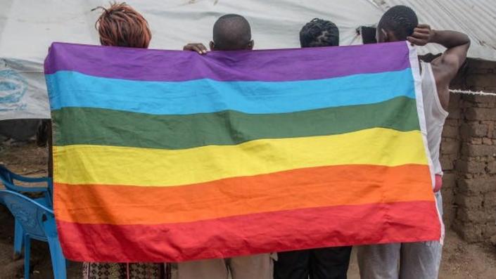 Image shows refugees holding up a rainbow flag