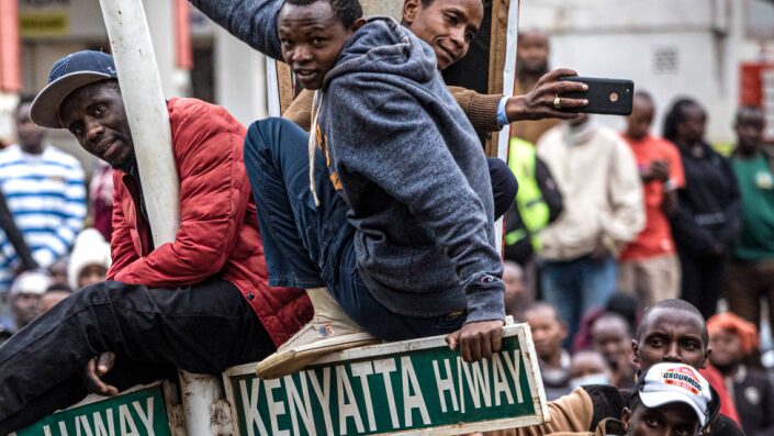 People at a rally in Kenya - with some sitting on a signpost - 3 August 2022