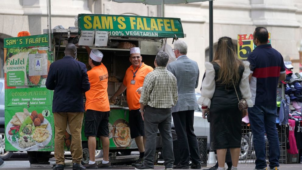 Emad Ahmed, center facing camera, works at his falafel cart in Zuccotti park in the financial district of New York, Tuesday, Sept. 13, 2022. It's becoming clearer that New York City's recovery from the pandemic will be drawn out and that some aspects