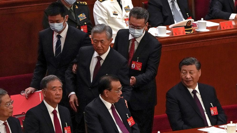 Chinese President Xi Jinping, right, looks on as former Chinese President Hu Jintao, standing at center, touches the shoulder of Premier Li Keqiang, center, as he is assisted to leave the hall during the closing ceremony of the 20th National Congress