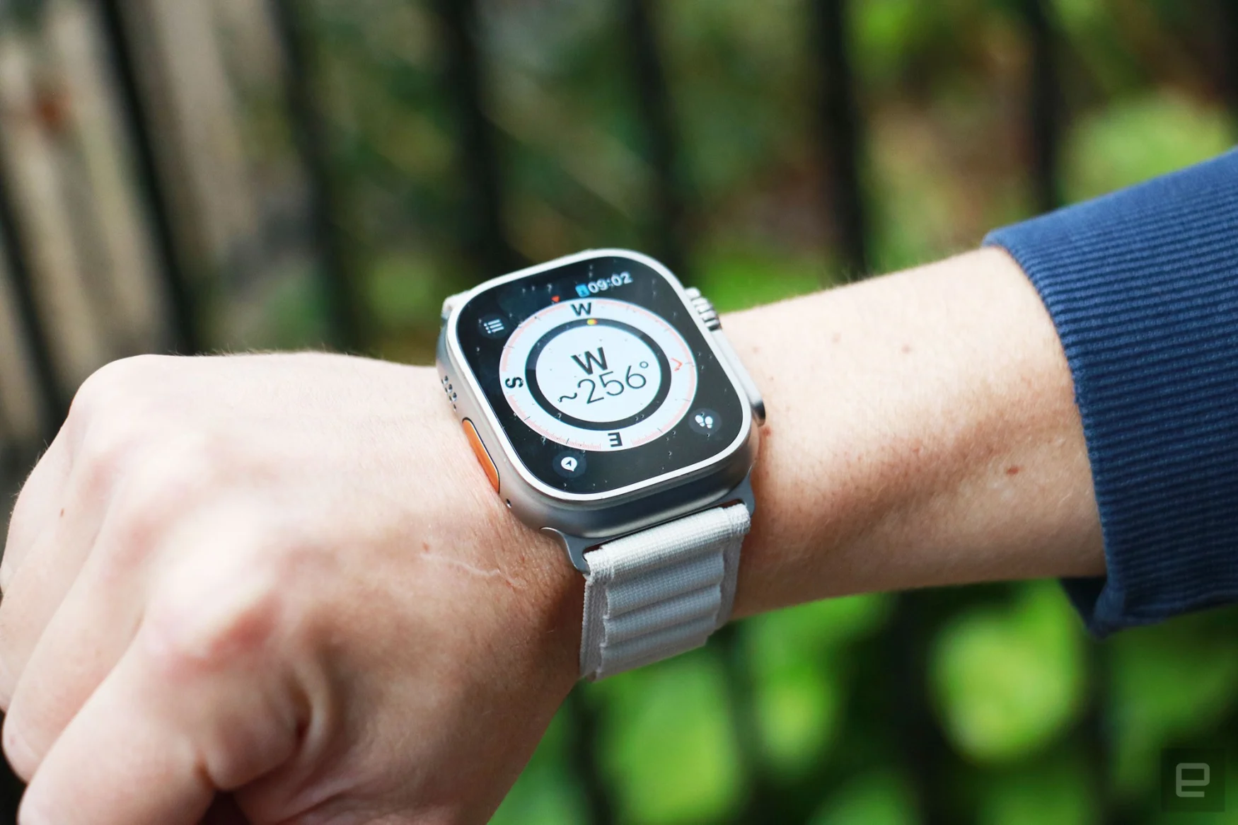 The Apple Watch Ultra on a wrist held in mid-air with a compass on its screen. The compass is showing the letter W with 