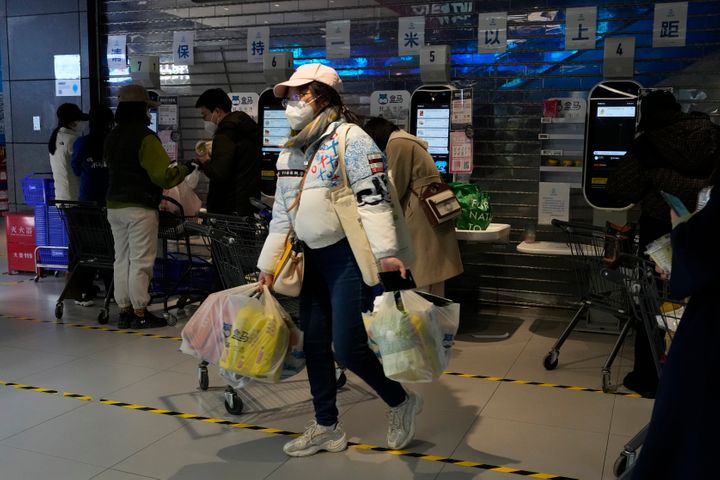 A resident carries her groceries near cashier machines at a supermarket in Beijing, on Nov. 25, 2022.