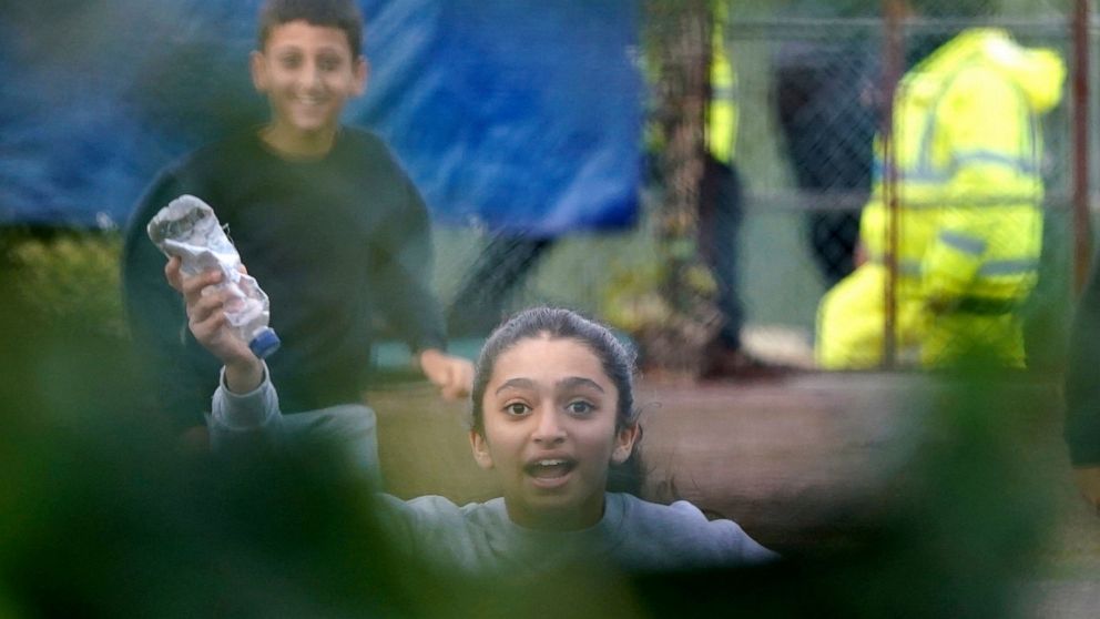 A young girl runs towards the fence carrying a message in a bottle inside the Manston immigration short-term holding facility located at the former Defence Fire Training and Development Centre in Thanet, England, Wednesday, Nov. 2, 2022. Details abou
