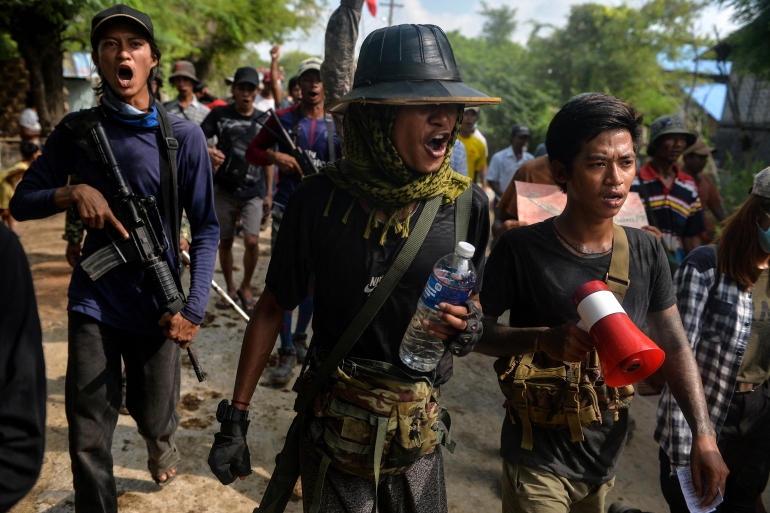 Men wearing green uniform, hardhats and carrying water, and loudpeakers, walk purposefully