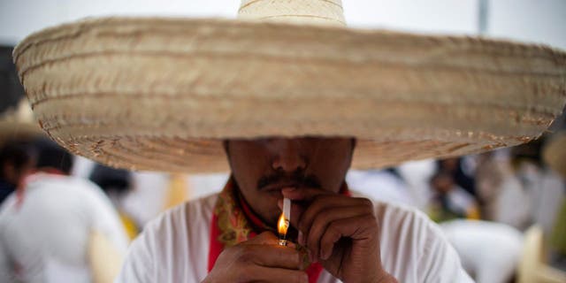 A man wearing a traditional Mexican lights a cigarette as he prepares to parade during the commemoration of the 112th anniversary of the Mexican Revolution at the Zocalo square in Mexico City on Nov. 20, 2022.