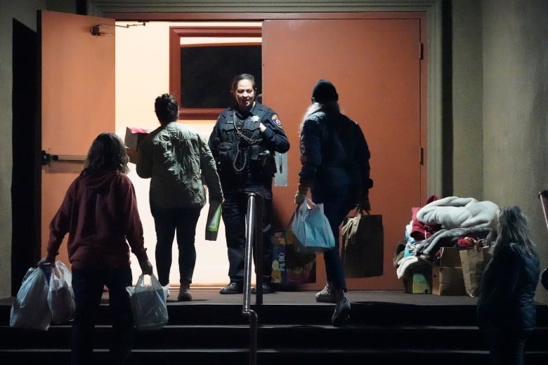 People carrying supplies in bags enter a family reunification centre after a shooting in Half Moon Bay, Calif. A female police officer stands at the door.