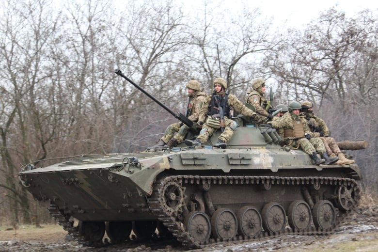 A military tank with 6 soldiers on top.