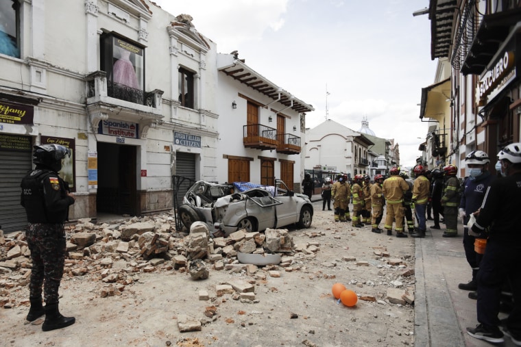 Rescue workers stand next to a car crushed by debris after an earthquake