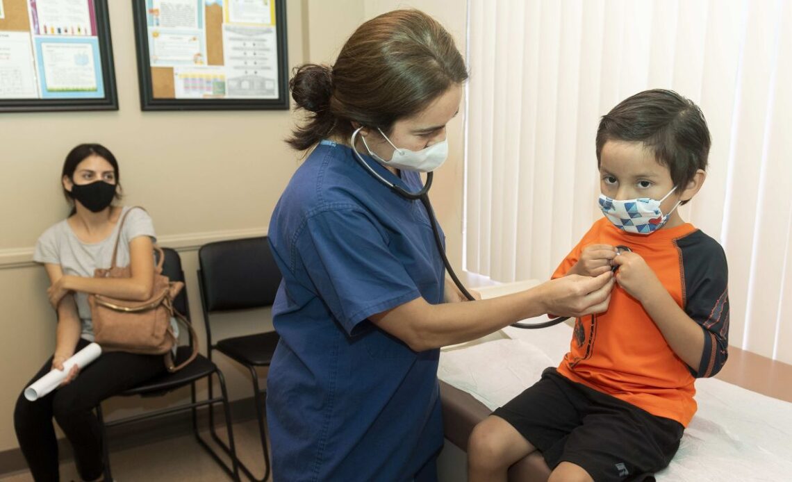 Dr. Kate Williamson listens to a child's heart during a yearly routine exam as his mom watches at Southern Orange County Pediatric Associates in Ladera Ranch, California, in July 2020.