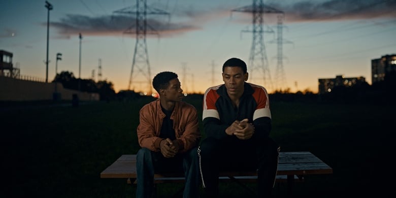 Two young men sit side by side on a picnic table at sunset.