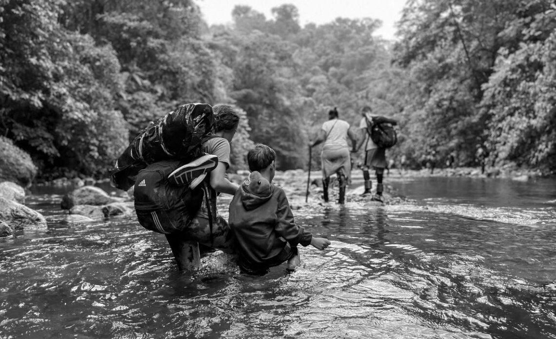 A Venezuelan woman guides her son through knee-high water, his dinosaur toy stuffed safely in his sweatshirt. She's hoping to get them to the US, to be reunited with her husband.