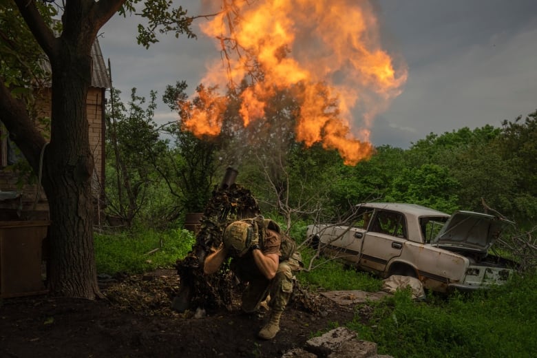 A soldier kneels and covers their ears as they fire a mortar round.