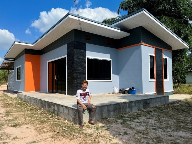 A man sits on a concrete slab outside a house.