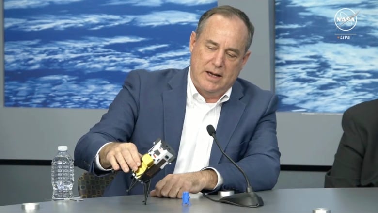 A person holds a miniature model spacecraft while sitting at a table.