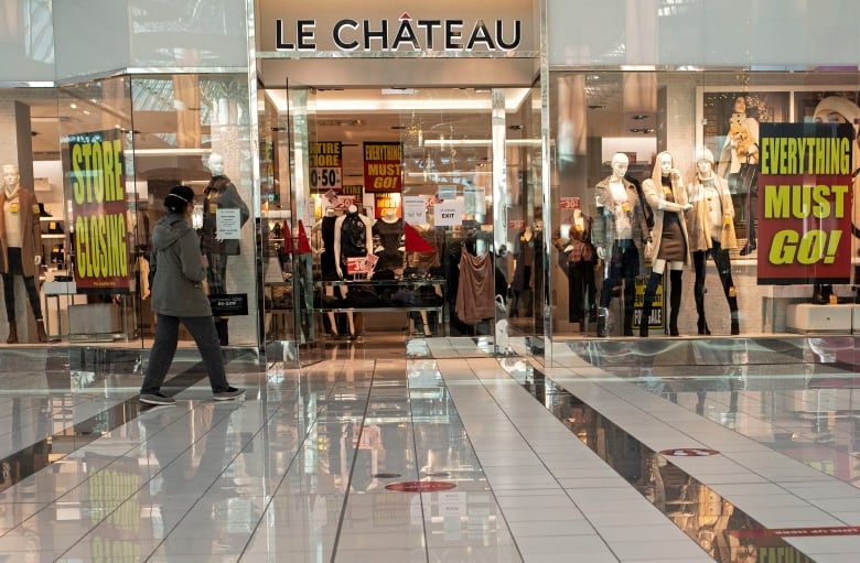 A woman in a face mask walks past Le Chateau, a clothing store, which has "Store closing" and "Everything Must Go!" signs on it.