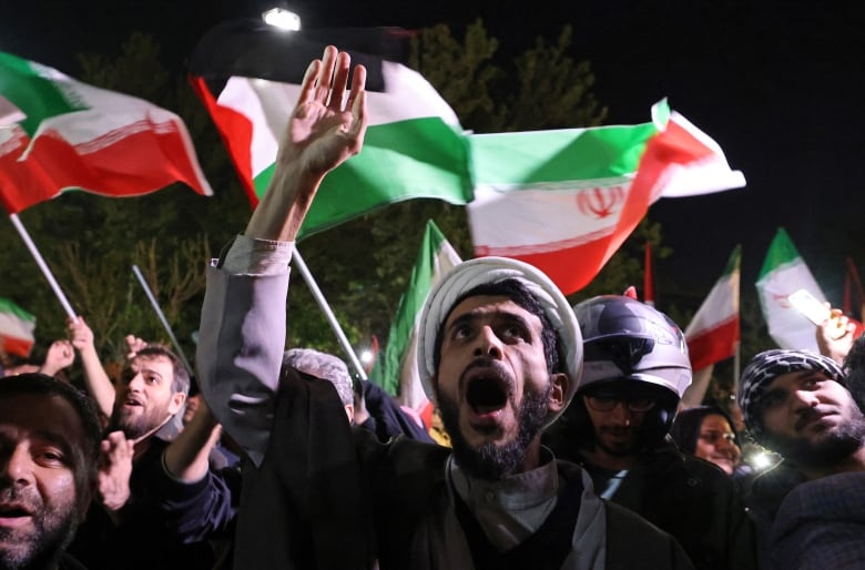 Men shout and wave Iranian and Palestinian flags in a demonstration.