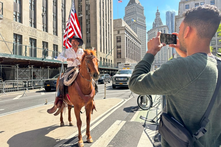 A man on a horse holds a US flag outside the Manhattan Criminal Courthouse.