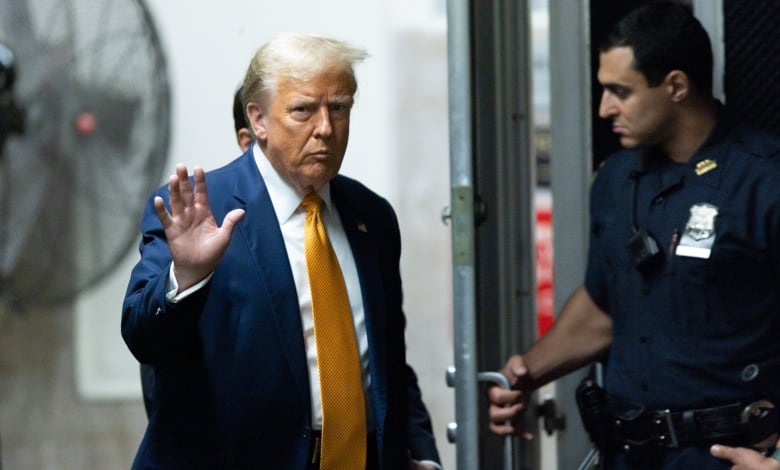 A man in a dark blue suit and orange tie waves.