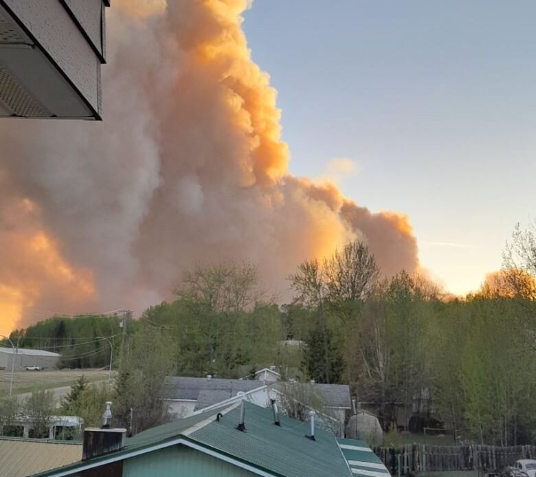 Large plumes of orange smoke are seen behind a row of houses.