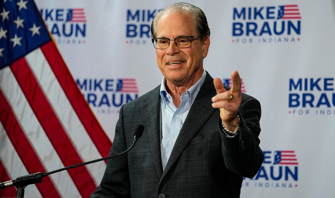 Sen. Mike Braun, gesturing with left hand in front of flag, campaign backdrop