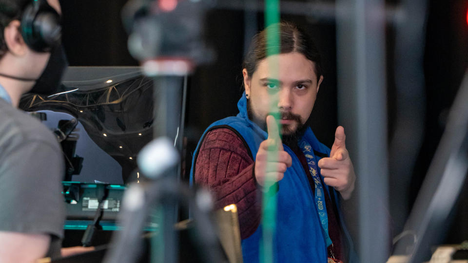 A person in a blue vest and red sweater makes finger guns at the camera at a recent Games Done Quick event.