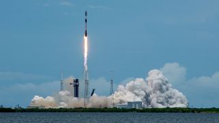 a black-and-white spacex falcon 9 rocket launches into a blue sky.