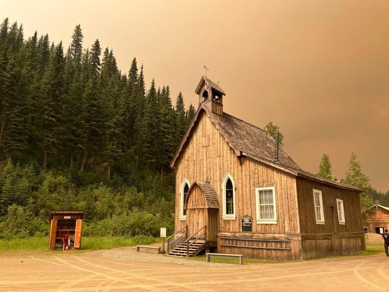 A rustic church with forest behind and wildfire smoke casting a pall over the town.