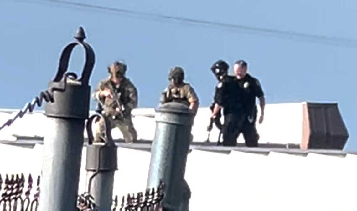 Law enforcement officers stand over the body of would-be Trump assassin, Thomas Crooks on the roof of a building