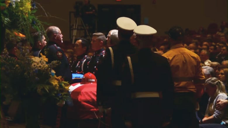 Firefighters line up beside a casket at a funeral.