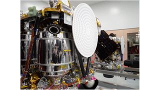 two shiny silver spacecraft sit inside a large white-walled clean room