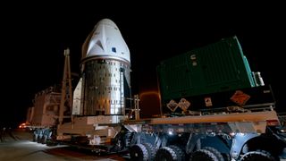 a white space capsule moves down a road at night on the back of a flatbed truck