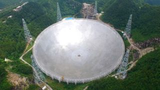 aerial view of a huge gray radio telescope built into a verdant landscape