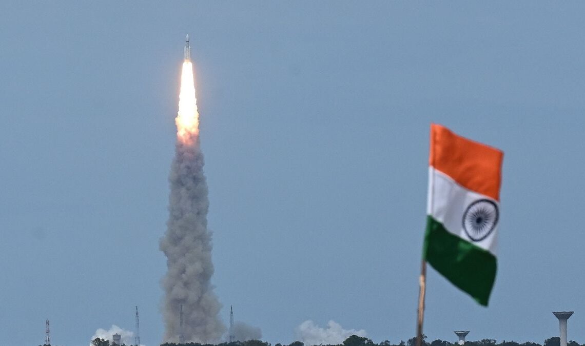 a rocket launches in the background behind an indian flag