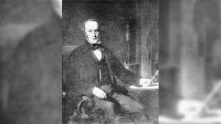 A black-and-white image of a white man sitting on a chair in a tuxedo