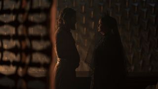 characters in brown robes talk to one another inside a stone temple