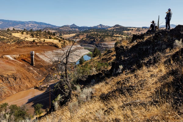 A view of the partially dismantled Iron Gate Dam on the Klamath River as a group of people on a hillside above watch.