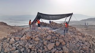 a group of people work at a desert excavation site under a tent