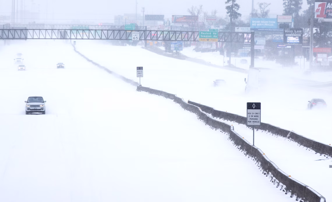 A few cars drive along a snowy interstate along a strip mall in Texas.