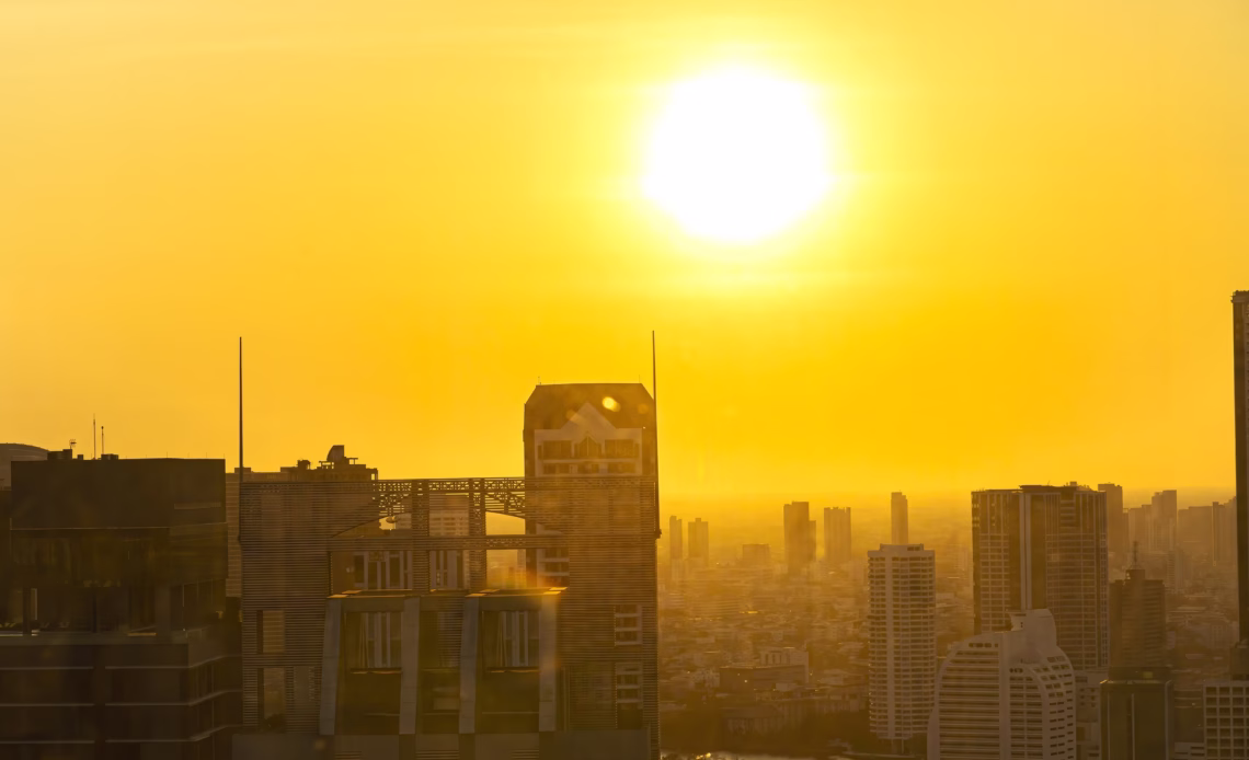 A cityscape with a very large, bright sun shining over it.